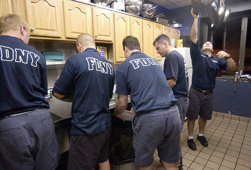 FIREHOUSE LIFE: Ladder 10 Company firefighter Chris Martucci hangs up a dish as (from right) Rob Barron of Ladder 15, Kevin Kelly of Ladder 10, John Thompson of Engine 4 and Dan Cavanaugh of Ladder 10 clean up after a nightly meal. Due the destruction endured by their 10 house across from the World Trade Center site, Ladder 10 has joined the South Street station, which already houses Engine 4 and Ladder 15.  Photo by Mike De Sisti 8/7/02 © 2002 Appleton Post-Crescent