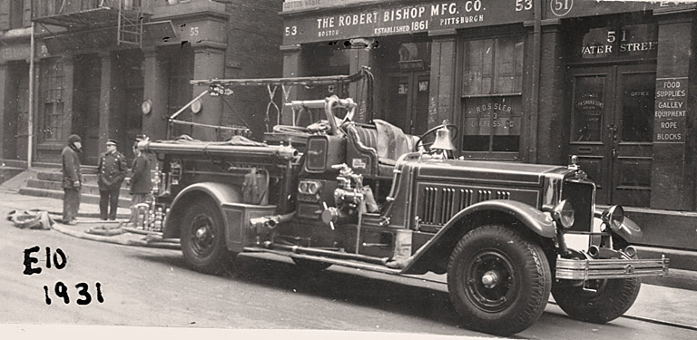 1931 American LaFrance 700 Gallon Pumper. Rig parked in street with hose flaked out from the back step. The officer appears to be talking with two civilians in the left of photo. Photo FDNY George F. Mand Library